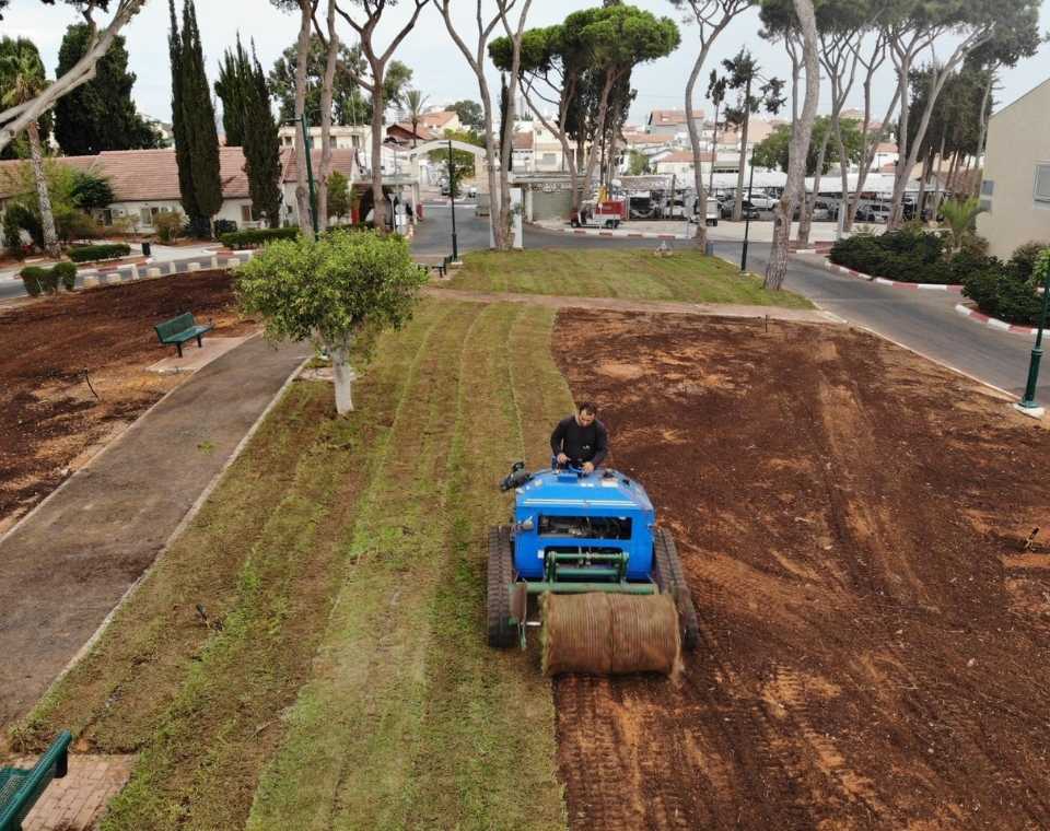 טרקטורון כחול מניח דשא חדש על מדשאה ציבורית, גינון וטיפוח גינה בישראל