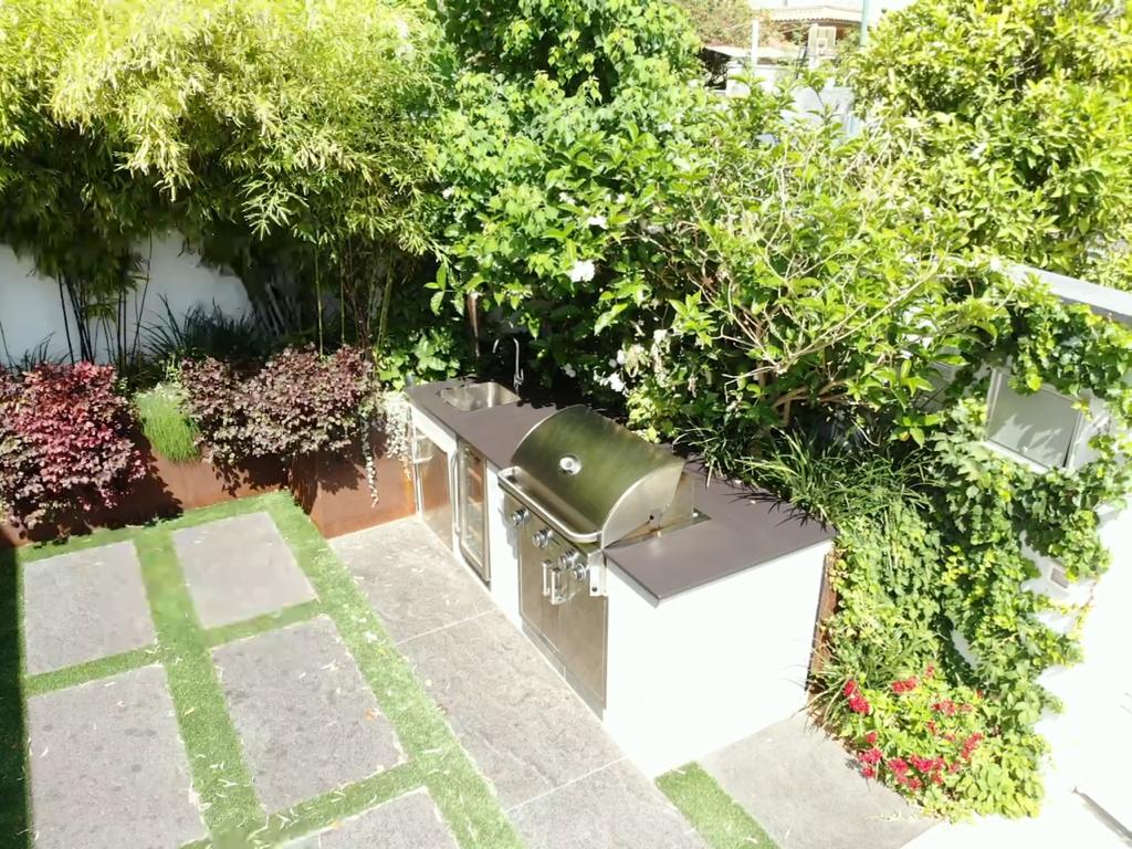 מטבח חוץ עם גריל גז מנירוסטה, כיור וגינה ירוקה מטופחת, מתאים לגינה פרטית