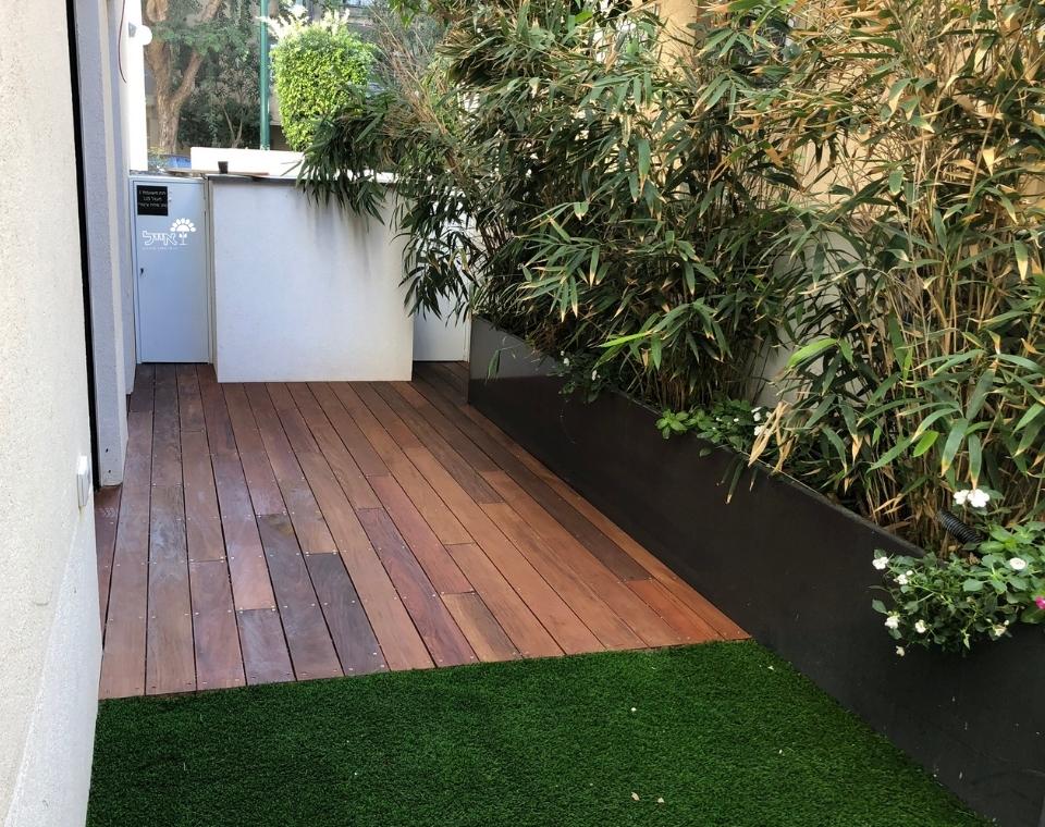 מרפסת עם דק עץ, דשא סינתטי, עציצי במבוק ופרחים לעיצוב גינה ביתית