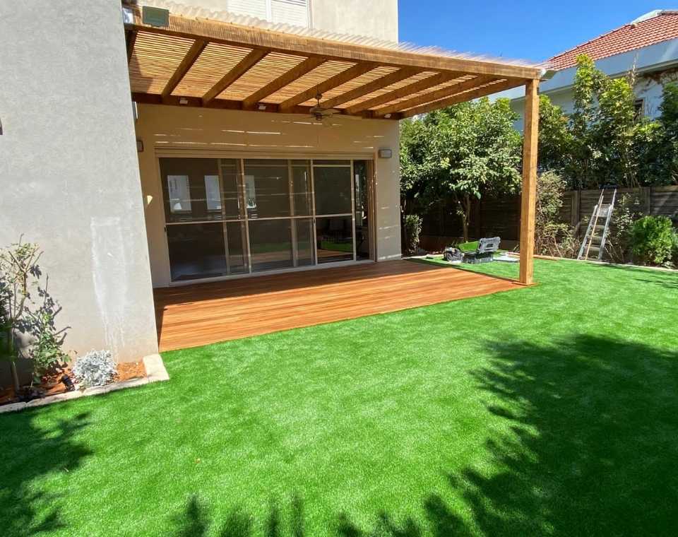 דק עץ מרפסת עם פרגולה ודשא סינטטי בחצר בית פרטי, גינה מטופחת